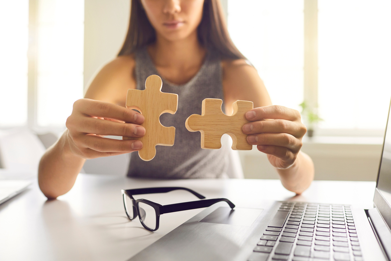 Close-up of Businesswoman Joining Two Pieces of Jigsaw Puzzle as Metaphor for Finding Solution
